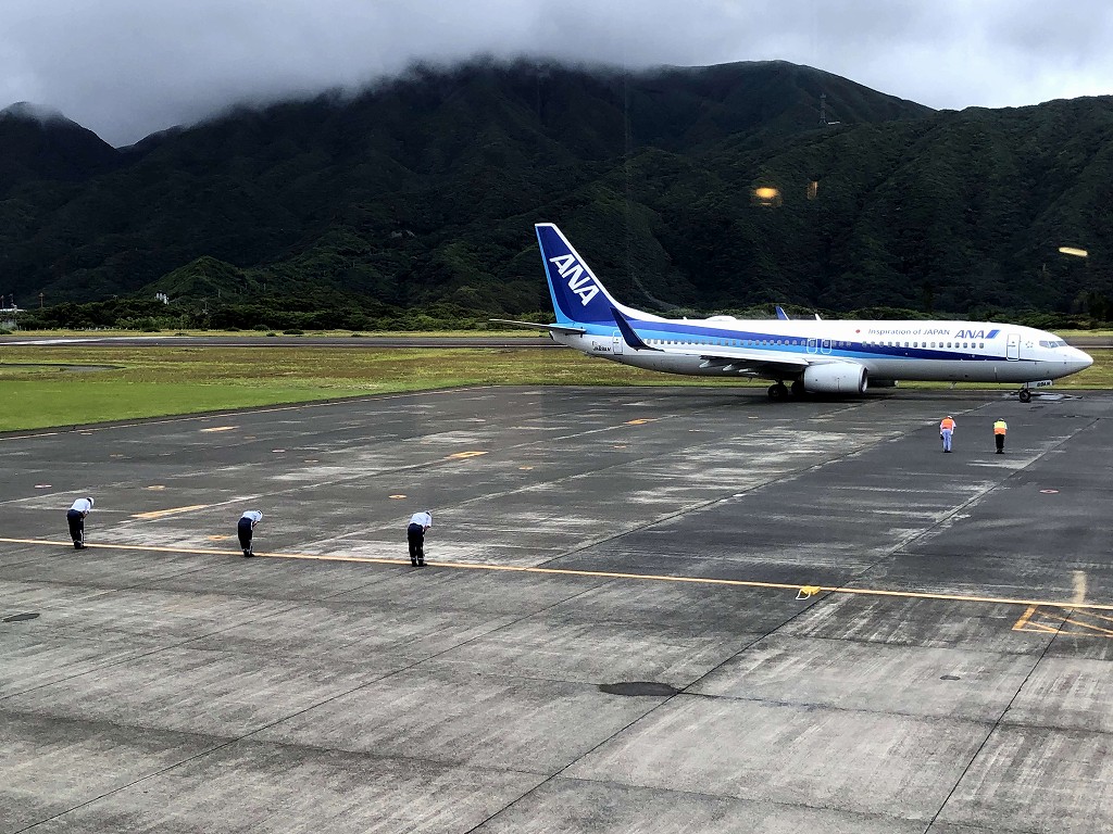 八丈島空港を飛び立つ飛行機に敬礼する整備士